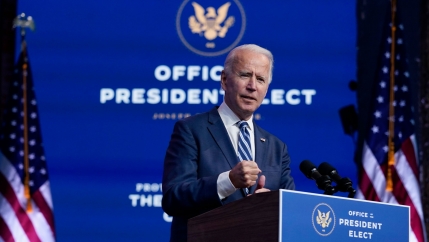 US President-elect Joe Biden is shown standing at a podium with microphones in front of a backdrop that says, 
