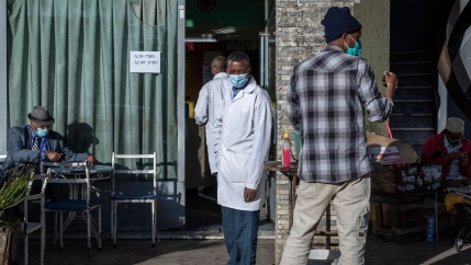 Several people are shown standing and sitting at a tea room with several wearing face masks.