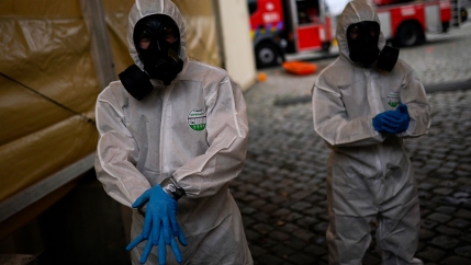 To people are shown dressed in medical protective gear including full facemasks and blue gloves.