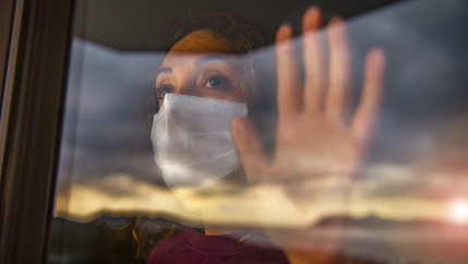 A woman with a mask looks out a window.