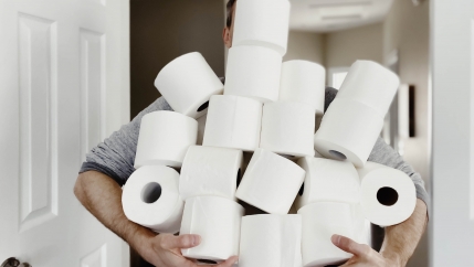 A man holds a large stack of toilet paper rolls. 