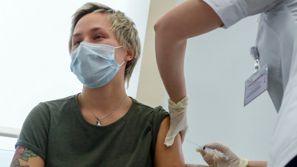 A person is shown with their shirt sleeve rolled up and receiving an injection in their shoulder by a medical professional.