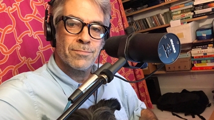 Marco Werman is shown with a microphone and his dog Frankie sitting on his lap.