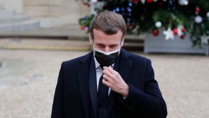 French President Emmanuel Macron is shown wearing a face mask and dark suit while standing outside.