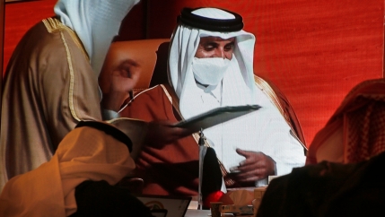 Two people are shown from behind wearing head coverings and looking up at a screen showing with Qatar's Emir Sheikh Tamim bin Hamad Al Thani.