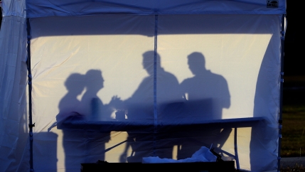 The silhouette of four people are show against the white panel of a tent.