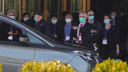 A large group of people from the WHO are shown wearing face masks with a car in the nearground.