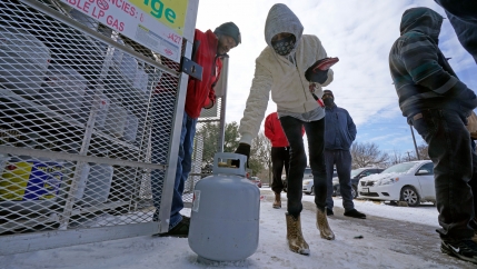 A woman is shown bending over with a white propane tank in her hand and wearing a hooded jacket.