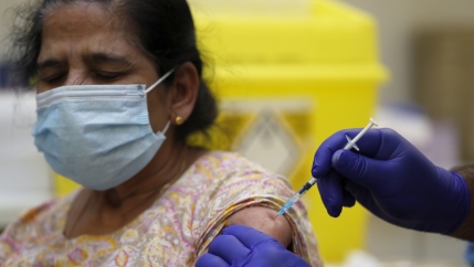 An Indian British woman wears a face mask and receives a shot in her arm with someone wearing purple gloves.