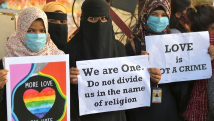 Three women protestors hold up signs reading 