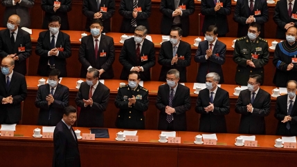 Chinese President Xi Jinping is shown wearing a dark suit and walking past several rows of men all applauding him.