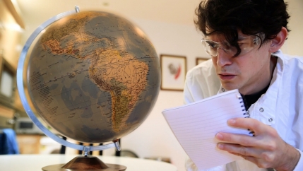 A man wearing glasses looks at a globe. 