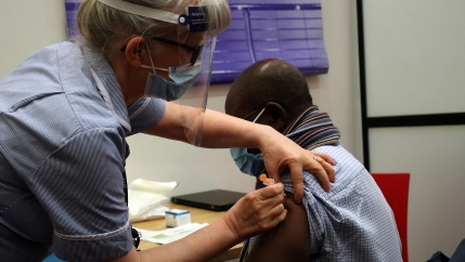 A man is shown with his left sleeve raised and a medical professional injecting a syringe into his arm.