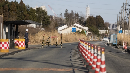 Security guards look at outbound vehicles moving toward them at a security checkpoint where part of the Fukushima Daiichi nuclear power plant is seen in the background in Okuma town in Fukushima prefecture, northeastern Japan, Feb. 25, 2021. An official