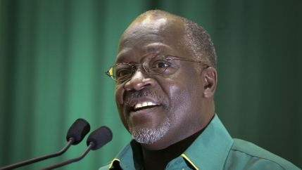 John Magufuli wears glasses a green shirt and speaks at a podium with a green background 