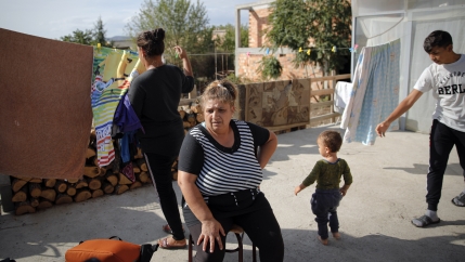 A woman with a black and white striped shirt sits outside with younger children surrounding her. 