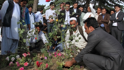 A group of men gather around a memorial to plant flowers for victims of a militant attack. 