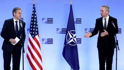 NATO Secretary General Jens Stoltenberg (R) and US Secretary of State Antony Blinken are shown standing opposite each other with the US and NATO flags in the background.