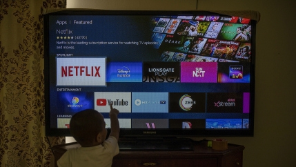 A child looks up at a TV screen with several apps to choose from at his home in New Delhi, India. 