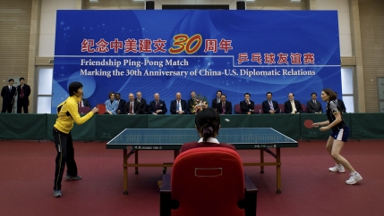 Table top tennis players compete in front of a large blue banner