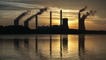 Smoke billows from stacks against a setting sun. 