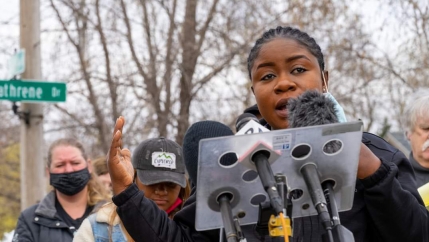 A woman speaks at a podium representing Black Immigrant Collective. 