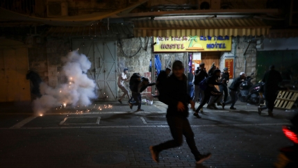 Several people are shown under the dark of night running from sparks and smoke.