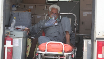 An older man is shown sitting on a gurney with a face mask on supplying oxygen.