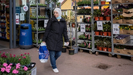 Asmaa al-Natour wears a hijab and black jacket and sjeans while holding a plastic bag and shopping at a flower store in Denmark.
