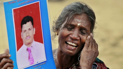 A woman weeps while holding a picture of her dead son, with a hand to her cheek, and eyes closed. 