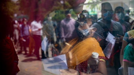 A woman wearing a yellow sari is shown through a window with her head leaned back and long swab in her nose.