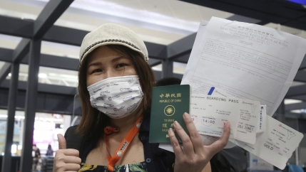 A Taiwanese woman wearing a mask and a white hat holds her passport and airline tickets before she boards a plane. 