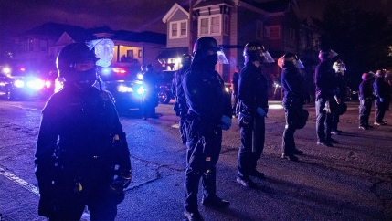 Police at night lining the street with police cars in the background with their lights on