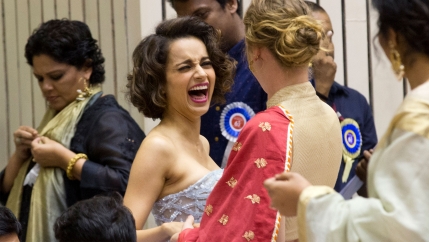 Woman in white dress laughs while talking to woman facing away from camera in red dress