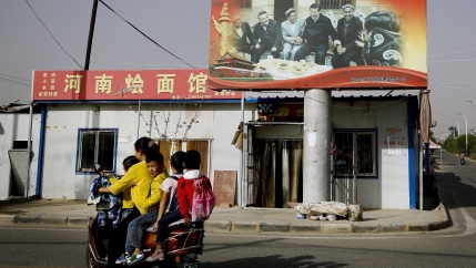 Children ride on a motorcycle near a large billboard. 