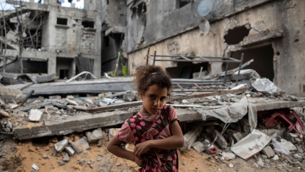 Girl stands in front of destroyed buildings