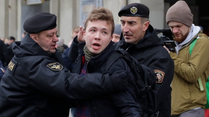 Raman Pratasevich is shown in a dark jacket with a police officer holding him on either side.