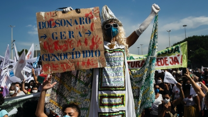 A man walking on stilts holds a sign with a message that reads in Portuguese: 