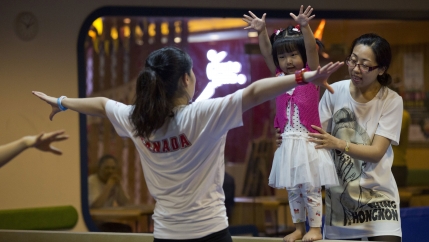 A child is supported on the balance beam during classes at a gym