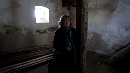 A woman stands in an abandoned building with light coming through the window. 