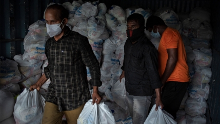 Men carrying white plastic bags of food from a pile of bags