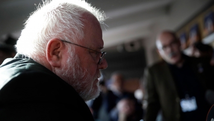 Cardinal Reinhard Marx, who has white hair and beard, is shown in a profile view wearing glasses and sitting.