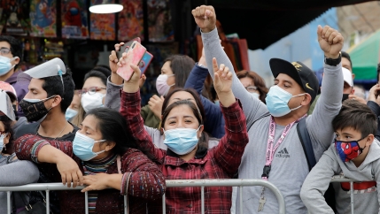 People wearing masks behind a barricade hold their hands and fists up in the air