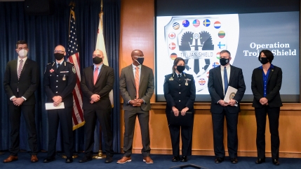 Law enforcement officials stand in front of an Operation Trojan Shield logo at a news conference