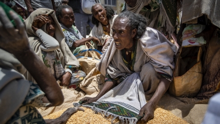 A woman argues over a pile of yellow lentils at a market. 