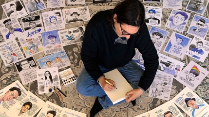 A man is shown sitting cross-legged with dozens of cartoons on the floor all around him.