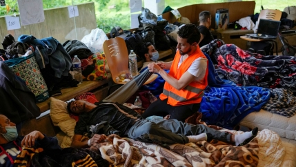 A man wearing a reflective orange vest is shown kneeling next to another man laying down on his back.