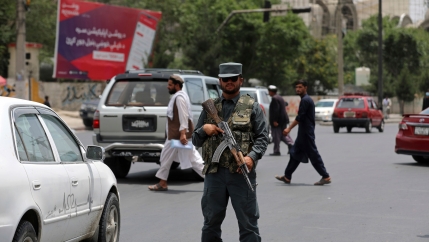 A policeman is shown wearing military fatigues, dark sunglasses and holding a Kalashnikov rifle.