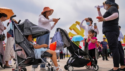Women gather with their children in strollers and the Chinese Communist Party logo in the background
