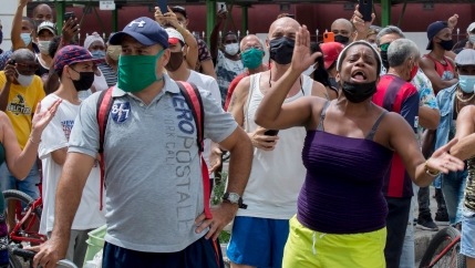 A woman wearing a purple shirt is shown with her hands out stretched and shouting among a large crowd of people.